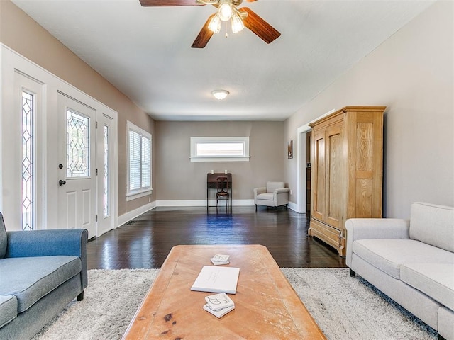 living area featuring baseboards, dark wood-type flooring, and a ceiling fan