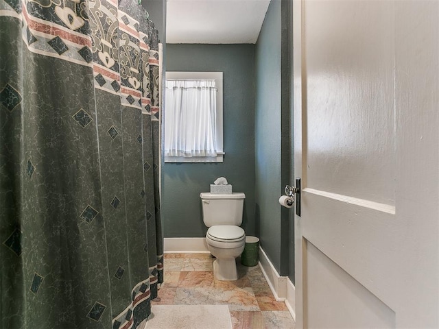 full bath featuring curtained shower, toilet, stone finish flooring, and baseboards