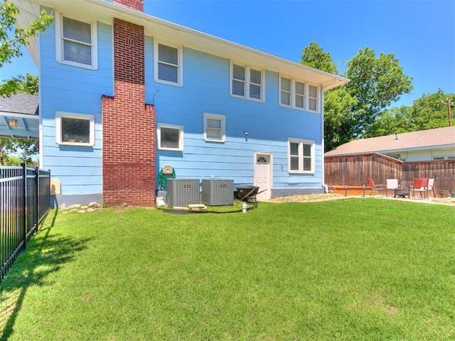 rear view of house featuring a lawn, central AC, and a fenced backyard