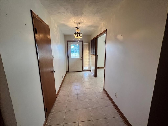 corridor featuring an inviting chandelier, light tile patterned flooring, baseboards, and a textured ceiling