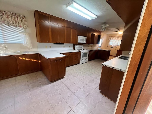 kitchen featuring white appliances, a peninsula, a sink, ceiling fan, and light countertops