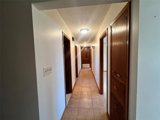 hall with light tile patterned floors, baseboards, visible vents, and a textured ceiling