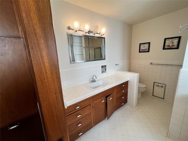 bathroom with a wainscoted wall, toilet, tile walls, tile patterned flooring, and vanity