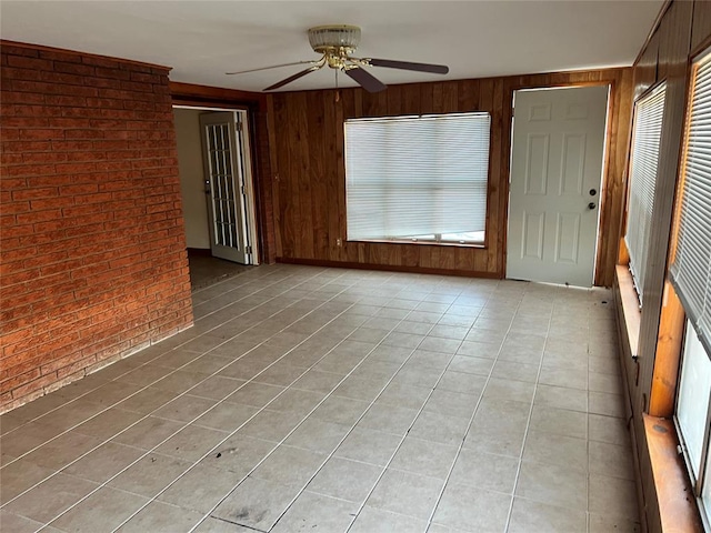 unfurnished room with light tile patterned flooring, wood walls, brick wall, and ceiling fan