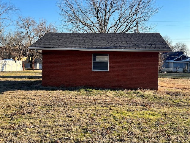 view of property exterior featuring brick siding, a shingled roof, a yard, and fence