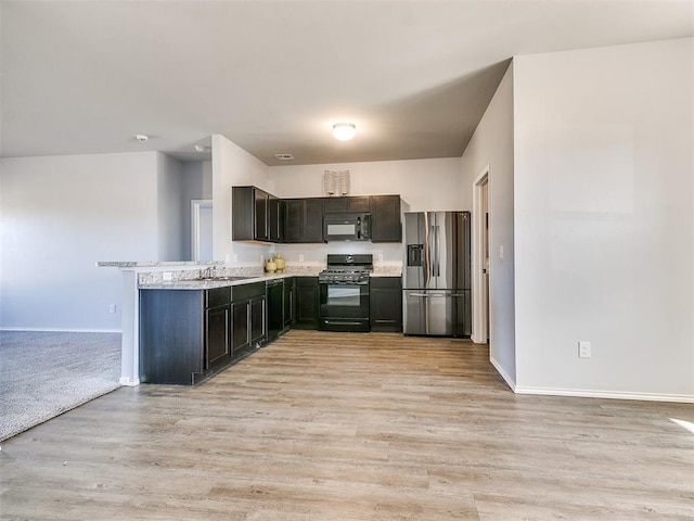 kitchen featuring light countertops, a peninsula, light wood-style floors, black appliances, and a sink