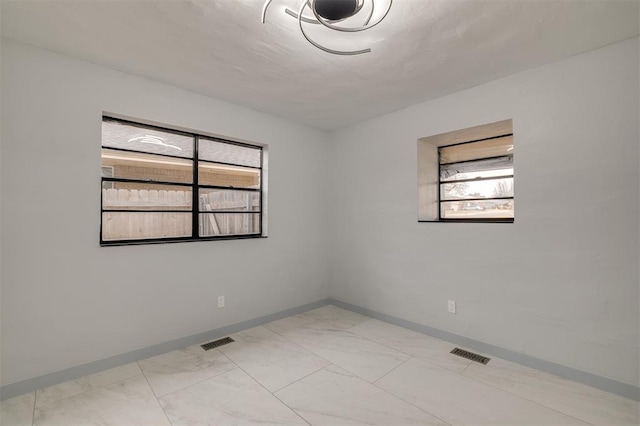 empty room with plenty of natural light, visible vents, marble finish floor, and baseboards