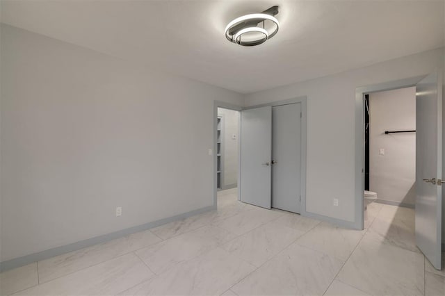 unfurnished bedroom featuring a closet, marble finish floor, ensuite bath, and baseboards