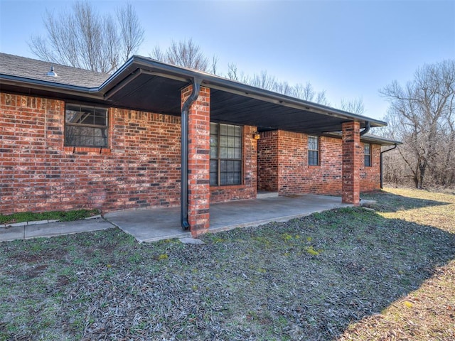 view of side of home featuring a patio, brick siding, and a lawn