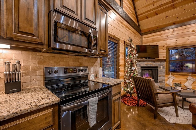 kitchen featuring decorative backsplash, wooden walls, light stone counters, and stainless steel appliances