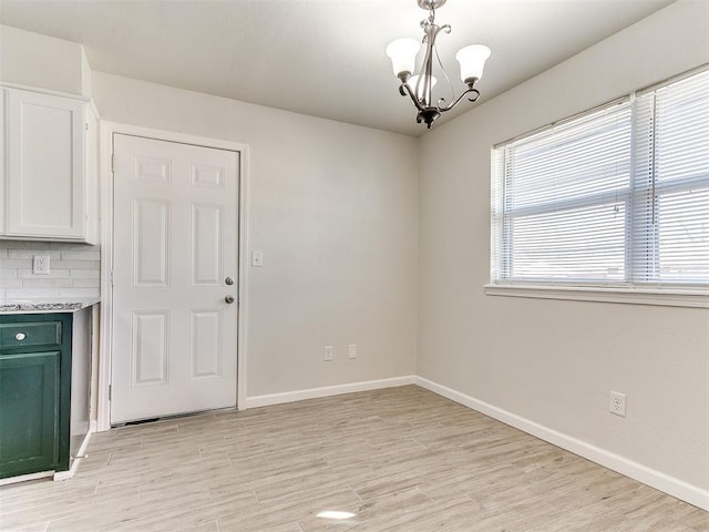 unfurnished dining area with a notable chandelier, baseboards, and light wood-style floors