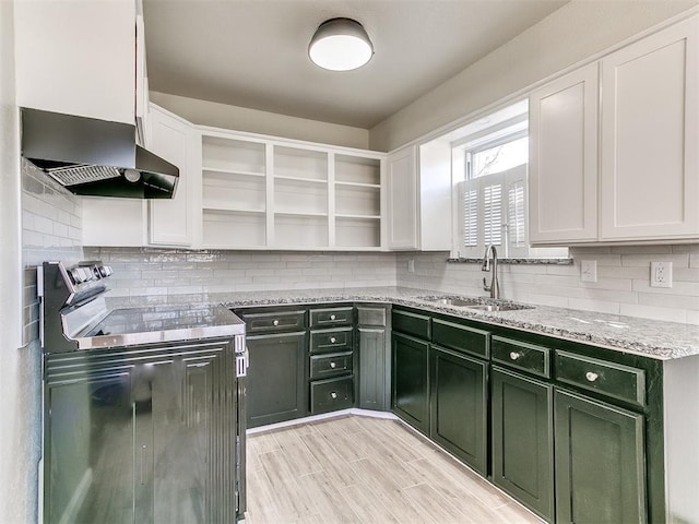 kitchen with light stone countertops, open shelves, a sink, green cabinets, and wall chimney exhaust hood