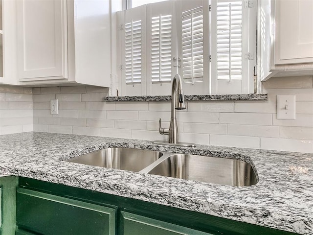 interior details featuring a sink, light stone counters, tasteful backsplash, and white cabinetry