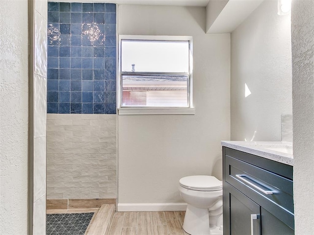 bathroom with vanity, baseboards, wood tiled floor, tiled shower, and toilet