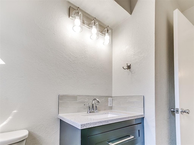 bathroom with decorative backsplash, toilet, vanity, and a textured wall