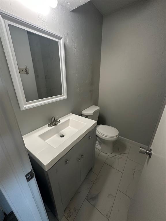 half bath with vanity, toilet, baseboards, and marble finish floor