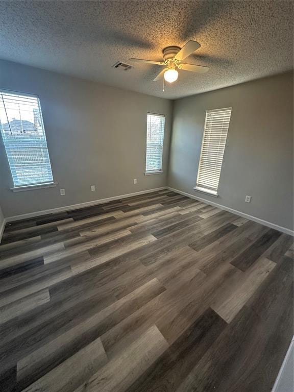 empty room featuring visible vents, baseboards, ceiling fan, dark wood-style floors, and a textured ceiling