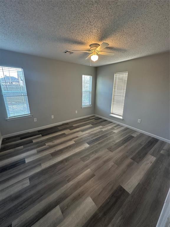 unfurnished room with a textured ceiling, dark wood-style floors, visible vents, and baseboards