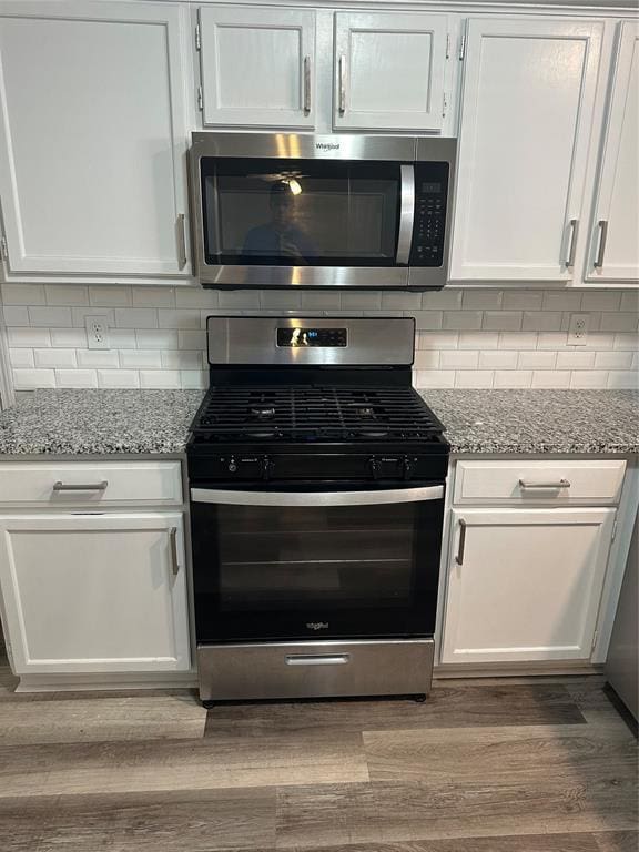 kitchen featuring wood finished floors, light stone countertops, backsplash, and stainless steel appliances