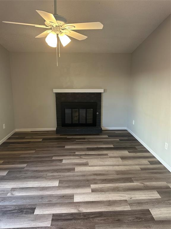 unfurnished living room with a glass covered fireplace, wood finished floors, baseboards, and a ceiling fan