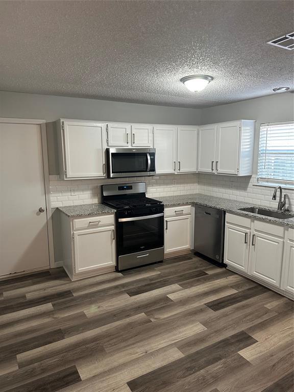 kitchen featuring dark wood finished floors, light stone counters, white cabinets, stainless steel appliances, and a sink