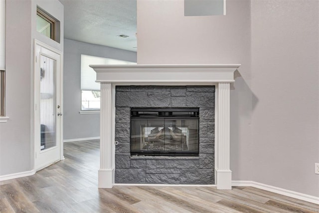 details with visible vents, baseboards, wood finished floors, a glass covered fireplace, and a textured ceiling