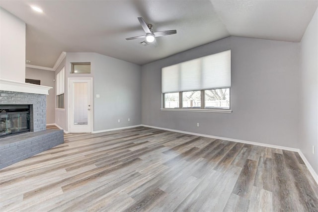 unfurnished living room featuring lofted ceiling, a brick fireplace, wood finished floors, and baseboards