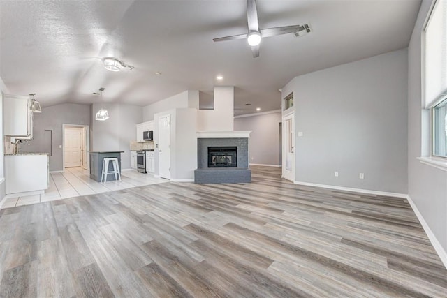 unfurnished living room featuring a brick fireplace, baseboards, light wood-type flooring, vaulted ceiling, and a ceiling fan