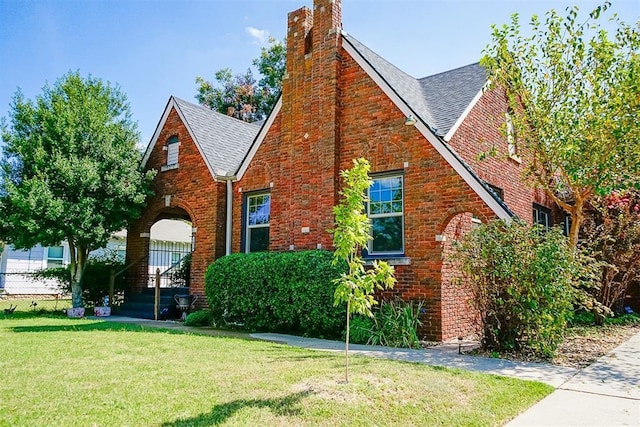 view of front of property featuring brick siding, a chimney, a front lawn, and roof with shingles