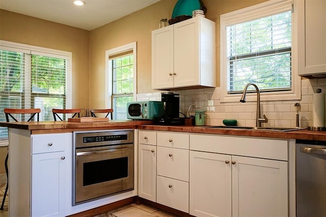 kitchen with a peninsula, a sink, decorative backsplash, stainless steel appliances, and white cabinets