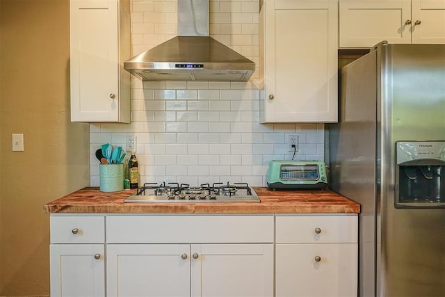kitchen with butcher block countertops, appliances with stainless steel finishes, white cabinetry, wall chimney exhaust hood, and backsplash