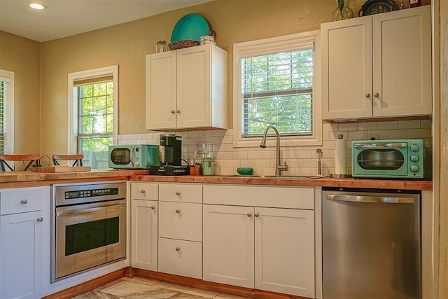 kitchen with a sink, white cabinetry, stainless steel appliances, a peninsula, and decorative backsplash