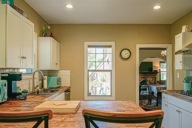 kitchen with tasteful backsplash, a fireplace, white cabinetry, wood counters, and a sink