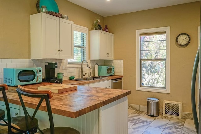 kitchen with visible vents, butcher block countertops, a peninsula, white cabinetry, and a sink