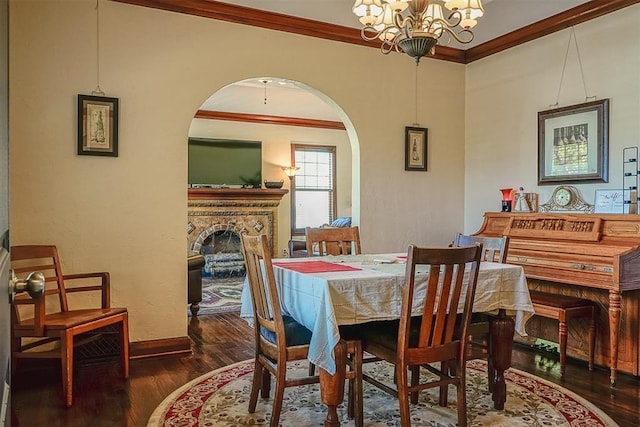 dining room with wood finished floors, a fireplace, arched walkways, ornamental molding, and a chandelier
