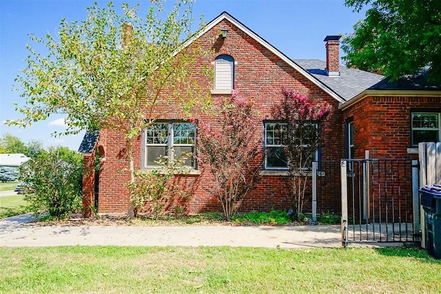 view of side of property with a yard, brick siding, roof with shingles, and a chimney