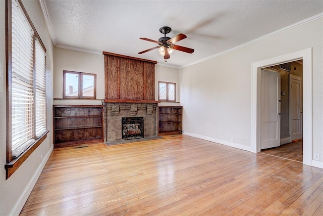 unfurnished living room with baseboards, ornamental molding, a stone fireplace, light wood-style floors, and a textured ceiling