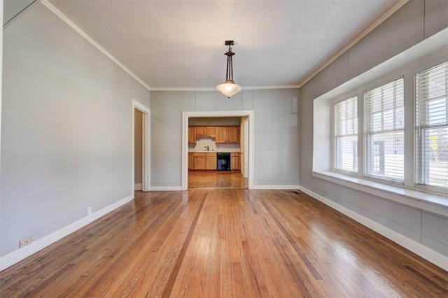 unfurnished dining area featuring crown molding, light wood-type flooring, and a textured ceiling