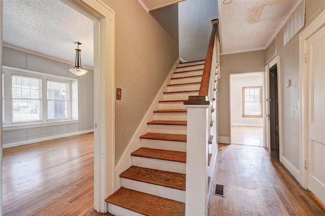 stairway featuring visible vents, crown molding, baseboards, wood finished floors, and a textured ceiling