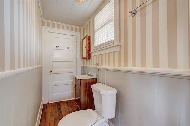 half bath featuring a wainscoted wall, toilet, wallpapered walls, and vanity