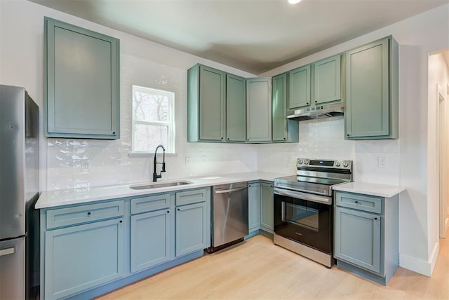 kitchen with light wood-style flooring, a sink, under cabinet range hood, appliances with stainless steel finishes, and decorative backsplash