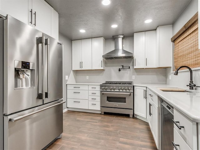 kitchen featuring a sink, wood finished floors, stainless steel appliances, wall chimney exhaust hood, and light countertops