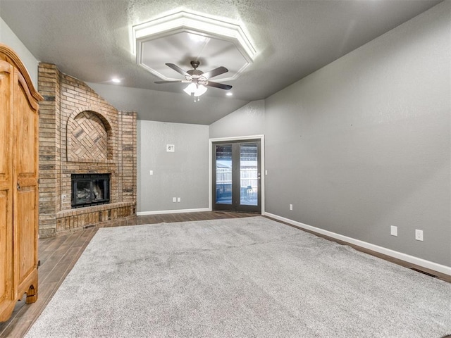 unfurnished living room featuring wood finished floors, lofted ceiling, a fireplace, ceiling fan, and a textured ceiling