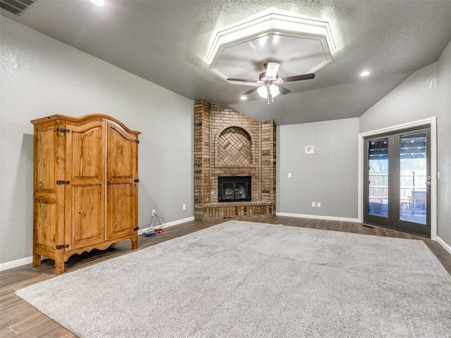 unfurnished living room featuring a ceiling fan, a textured ceiling, wood finished floors, a fireplace, and lofted ceiling