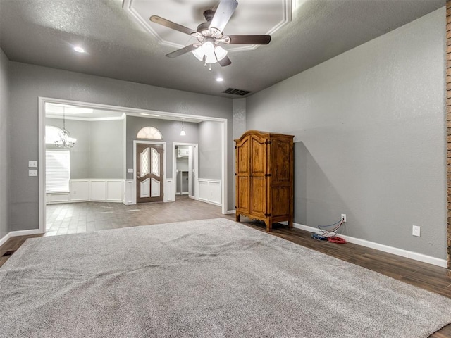 empty room with wood finished floors, baseboards, visible vents, a textured ceiling, and ceiling fan with notable chandelier