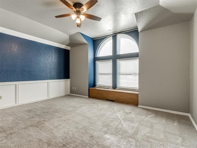 spare room with a wainscoted wall, carpet floors, a textured wall, a textured ceiling, and a ceiling fan