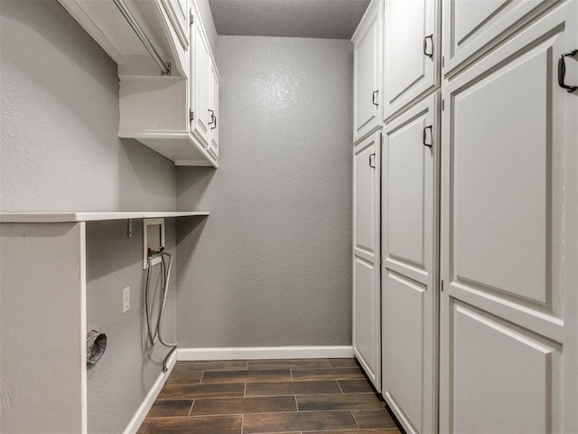 clothes washing area with a textured wall, cabinet space, baseboards, and wood tiled floor