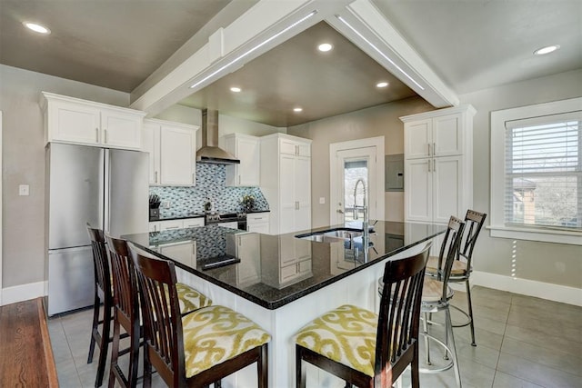 kitchen with a breakfast bar area, a sink, appliances with stainless steel finishes, wall chimney range hood, and tasteful backsplash