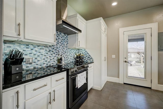 kitchen featuring dark stone counters, dark tile patterned flooring, white cabinets, black range with electric cooktop, and wall chimney range hood