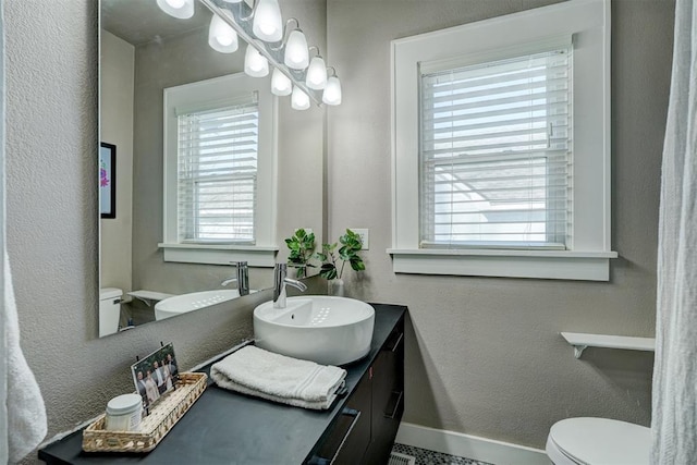 bathroom featuring vanity, toilet, a textured wall, and baseboards